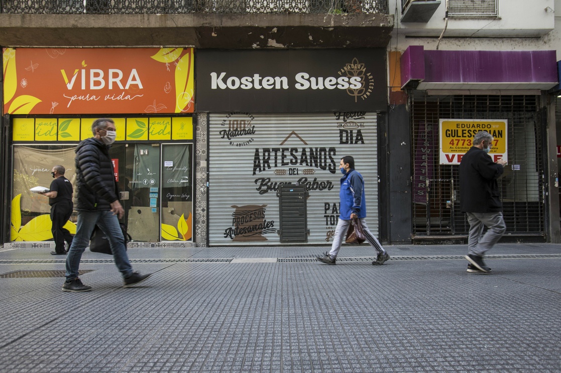 Personas caminan frente a locales comerciales cerrados de forma definitiva en la calle Florida, en la ciudad de Buenos Aires. Foto: La Jornada.