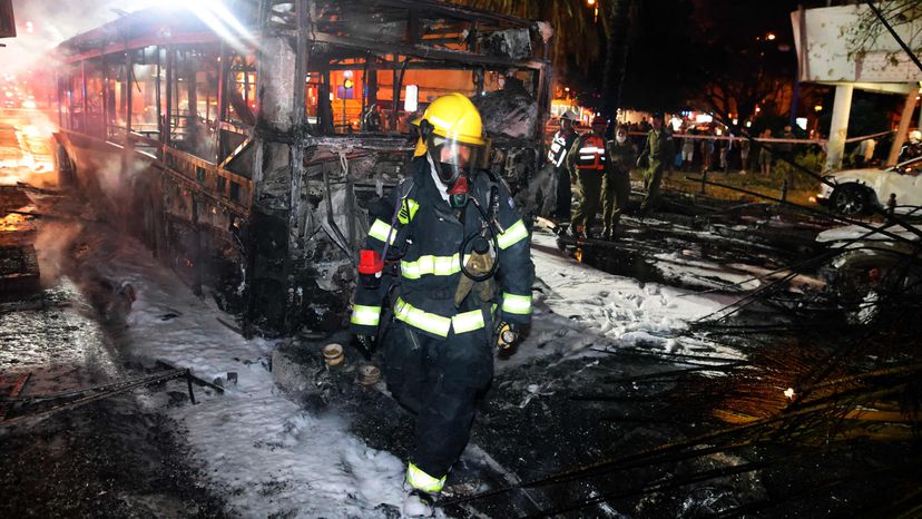 Personal de los servicios de emergencia israelíes alrededor de un autobús quemado en la ciudad de Jolón. Foto: El País.
