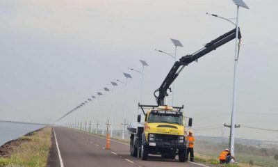 La Entidad Binacional Yacyretá (EBY) instaló un moderno sistema de iluminación en la zona de alto tránsito de la obra de maquinización del brazo Aña Cua, que hasta hace poco tiempo permanecía a oscuras. Se trata de la colocación de 150 unidades de columnas metálicas con paneles solares inteligentes, artefactos LED con brazos metálicos, soportes metálicos para los paneles solares y baterías ION de Litio, de marca Philips, firma internacionalmente conocida por la calidad de sus productos, informó la EBY Los módulos son de 56 LEDs por cada unidad, aumentando de esta forma la capacidad de iluminación de otros sistemas AP-LED ya existentes, instalados en procesos anteriores con módulos de solamente 12 LEDs por cada unidad. El flujo luminoso de los equipos es de 9.000 Lumen – 18.000 Lumen, mientras que los anteriores son de hasta 8.500 Lm. Los lentes ópticos de los equipos poseen un ángulo de hasta 60º – 140º. Estas 150 columnas instaladas y en funcionamiento, permiten programar su iluminación de modo a dividir la noche en cuatro períodos, de tal manera que las baterías funcionen con una vida útil prolongada. El sistema de alimentación en esta implementación es con baterías ION de Litio. Las fundaciones fueron construidas para la base de las columnas con 1,8 metros de profundidad, con una base de. 60×60 cm. Esto permitió mayor dosificación en la cantidad de material sólido instalado, que incrementa la resistencia de la base. Las columnas metálicas, por su alta calidad y resistencia, soportan mejor el impacto del viento que sopla con gran fuerza en la zona de embalse y en la Isla Yacyretá. Los costos pagados, incluyendo su instalación, los cálculos, planos y todo el acondicionamiento de puesta a punto, asciende a 3.200 dólares por cada unidad, que es el mismo precio abonado por la instalación de lumínicas hace dos años, en la zona de obras, específicamente en el tramo paso fronterizo hasta la Central Hidroeléctrica Yacyretá. Es importante recordar que, en los últimos dos años, los materiales y equipos importados vía transporte marítimo o aéreo, han sufrido altos sobrecostos, aun así, esto no afectó en ningún aspecto al proyecto. Esta situación se pudo sortear, en esta oportunidad, mediante la buena gestión para dotar de equipamiento de iluminación de primera calidad para dar mayor seguridad a los miles de obreros afectados a los trabajos de maquinización y que diariamente transitan por este lugar.