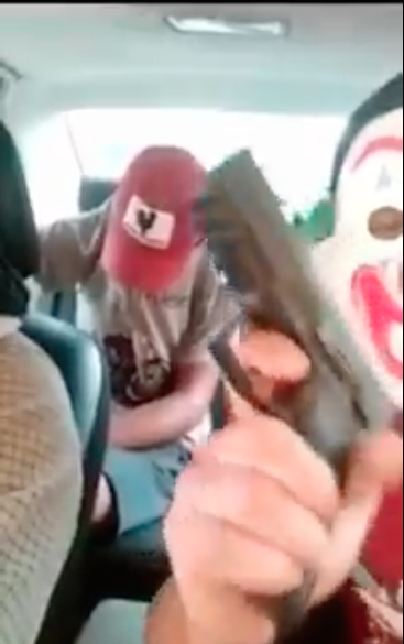 Uno de los integrantes tiene una máscara de payaso y muestra un arma. (Captura vídeo)