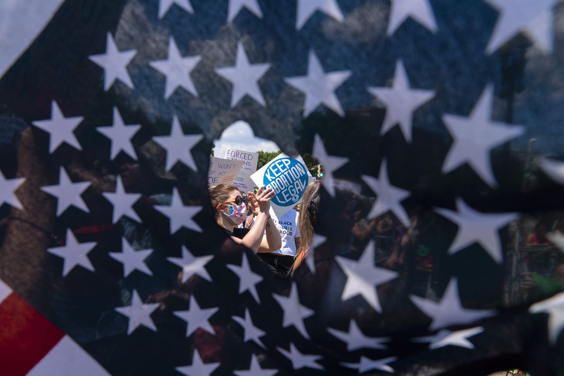 A través de un agujero en una bandera estadounidense, se observa a activistas que sostienen un letrero que dice "Mantengan legal el aborto", el 25 de junio de 2022, en Washington D. C. Foto: El País