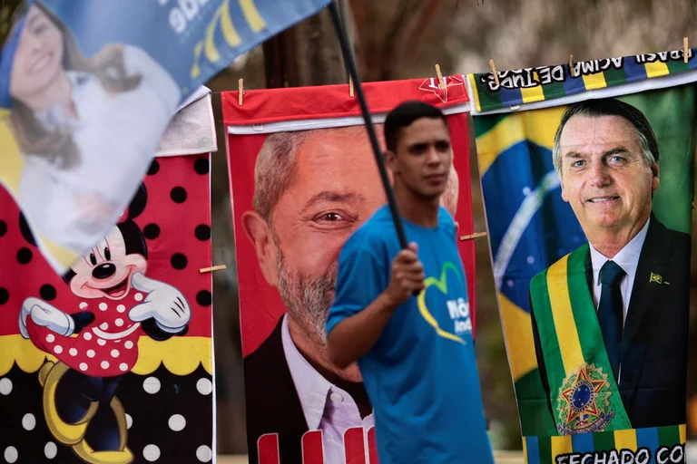 Un hombre con una bandera rodeado de toallas con las imágenes de Lula y Bolsonaro, Foto: Infobae,