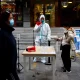 Un trabajador con traje de protección guía a las personas para que escaneen el código sanitario QR antes de someterse a la prueba de la enfermedad del coronavirus . Foto: Infobae