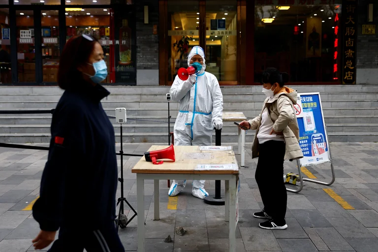 Un trabajador con traje de protección guía a las personas para que escaneen el código sanitario QR antes de someterse a la prueba de la enfermedad del coronavirus . Foto: Infobae