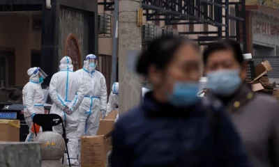 Residentes caminan cerca de los trabajadores de prevención en un complejo residencial cerrado en Beijing. Foto: Infobae