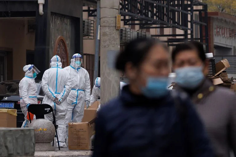 Residentes caminan cerca de los trabajadores de prevención en un complejo residencial cerrado en Beijing. Foto: Infobae