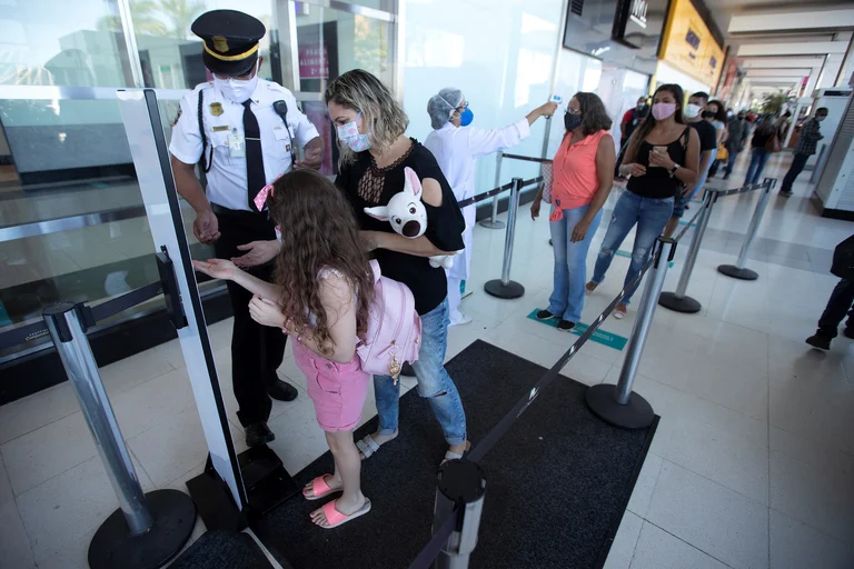 Un guardia aplica gel desinfectante a una mujer y a su hija, mientras otros ciudadanos esperan. Foto: Infobae