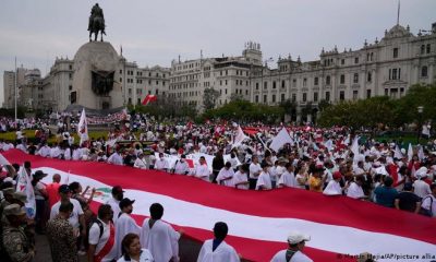 Manifestantes sostienen una gran bandera durante una marcha pidiendo por la paz, en la plaza San Martín en Lima. Foto: DW