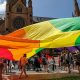 Manifestantes sostienen una bandera arcoíris gigante fuera de la Catedral de Santa María antes de la misa de réquiem pontifical por el cardenal George Pell. Foto:DW