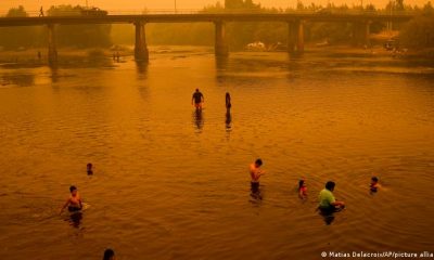 Personas vadean en el río bajo un cielo enrarecido por el denso humo de los incendios forestales, en Renaico. Foto: DW