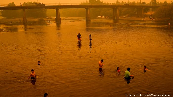 Personas vadean en el río bajo un cielo enrarecido por el denso humo de los incendios forestales, en Renaico. Foto: DW