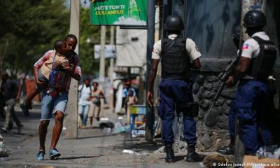 Un hombre corre con su hijo en brazos en medio de un operativo policial, en Puerto Príncipe, Haití. Foto: DW.