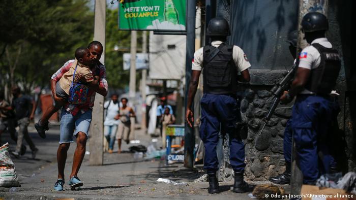 Un hombre corre con su hijo en brazos en medio de un operativo policial, en Puerto Príncipe, Haití. Foto: DW.