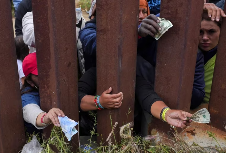 Migrantes buscan pagar a vendedores de comida del otro lado del muro. Foto: Infobae.