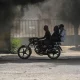 Una moto circula junto al humo de neumáticos ardiendo, durante una manifestación contra la inseguridad en Puerto Príncipe. Foto: DW.