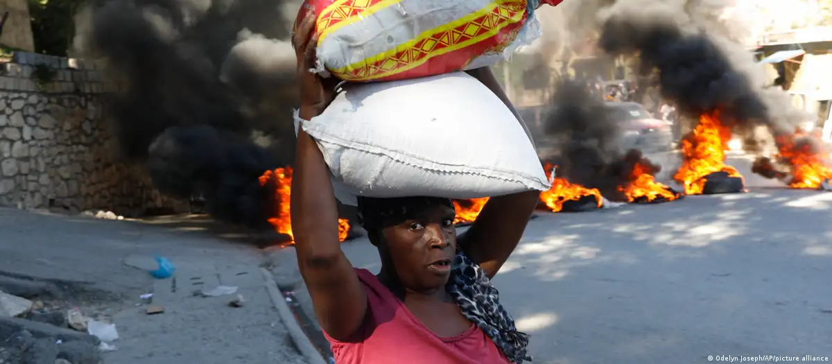 Una mujer pasa junto a neumáticos quemados por manifestantes en Puerto Príncipe, para llamar la atención sobre la inseguridad del país y exigir la renuncia del primer ministro Ariel Henry. Foto de archivo. DW.