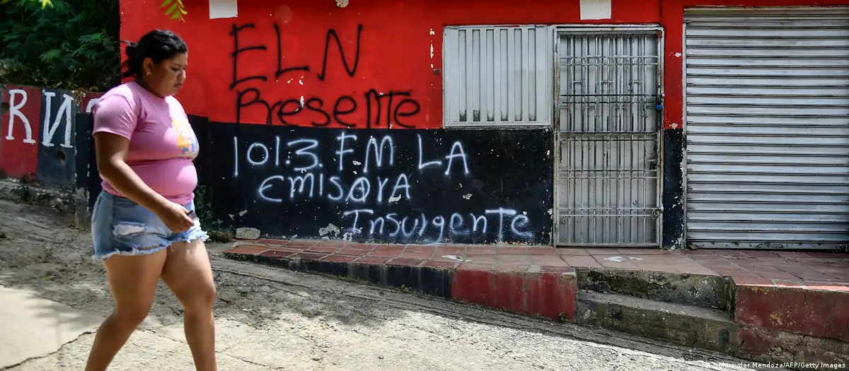 Una mujer camina frente a una pared con un lema del ELN en la región de Cúcuta, Colombia. Foto: DW.