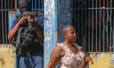 Mujer pasa frente a la vacía Prisión Nacional en Puerto Príncipe, Haití mientras un agente apunta con una metralleta sobre la cabeza de la transeúnteImagen: Odelyn Joseph/AP/