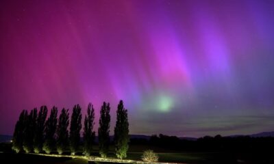 En esta fotografía de larga exposición, un auto circula por una carretera mientras las auroras boreales iluminan el cielo nocturno en Daillens, Suiza,