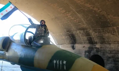 Un combatiente antigubernamental ondea una bandera de la oposición en la cabina de un avión militar del régimen sirio en el aeródromo militar de Kuweires, en la parte oriental de la provincia de Alepo, el domingo 01.12.2024. Imagen: AREF TAMMAWI/AFP