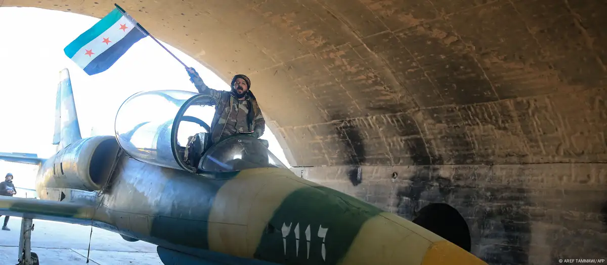 Un combatiente antigubernamental ondea una bandera de la oposición en la cabina de un avión militar del régimen sirio en el aeródromo militar de Kuweires, en la parte oriental de la provincia de Alepo, el domingo 01.12.2024. Imagen: AREF TAMMAWI/AFP