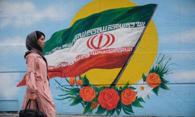 Una mujer camina frente a un mural con la bandera de Irán situado en una de las calles de Teherán. Foto: Infobae.