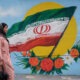 Una mujer camina frente a un mural con la bandera de Irán situado en una de las calles de Teherán. Foto: Infobae.