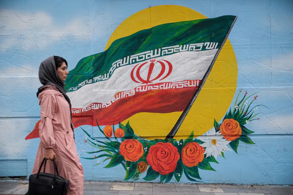 Una mujer camina frente a un mural con la bandera de Irán situado en una de las calles de Teherán. Foto: Infobae.